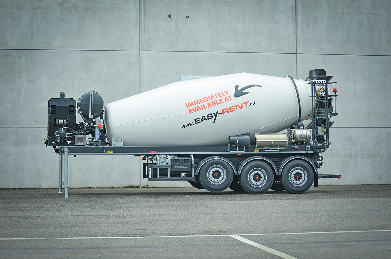 Side view of a 3-axle concrete mixer De Buf with auxiliary motor in front of a gray wall