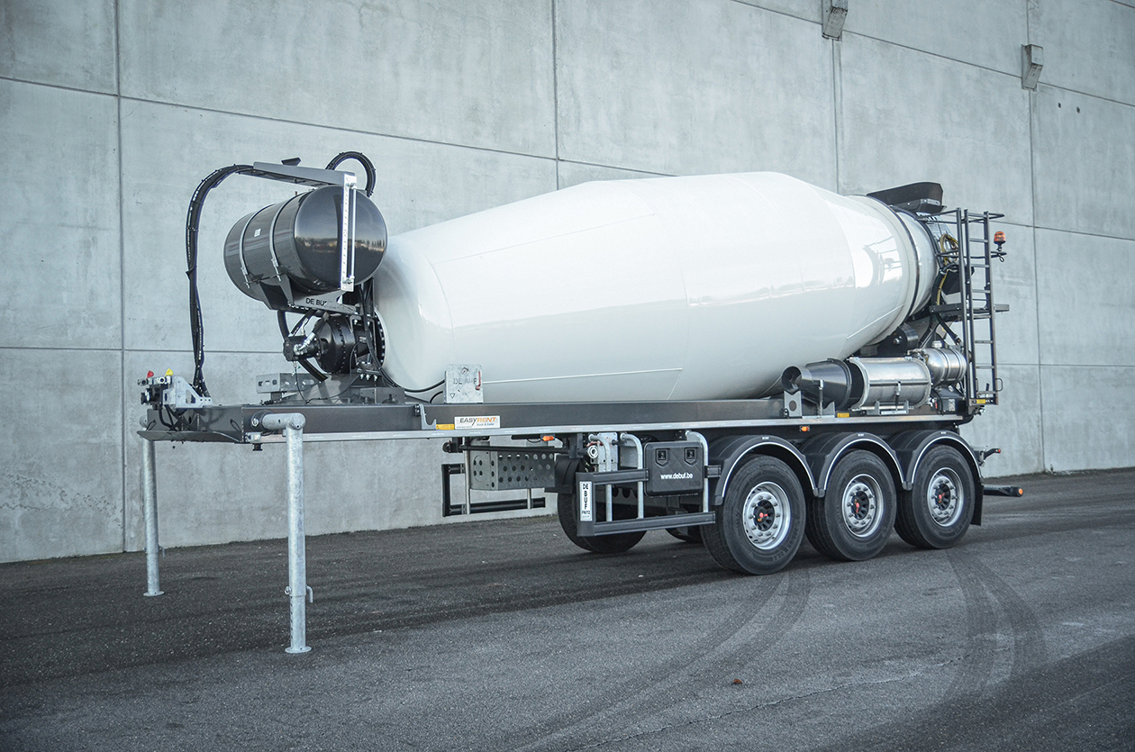 Front side view of a 3-axle concrete mixer trailer from the manufacturer De Buf in front of a gray wall