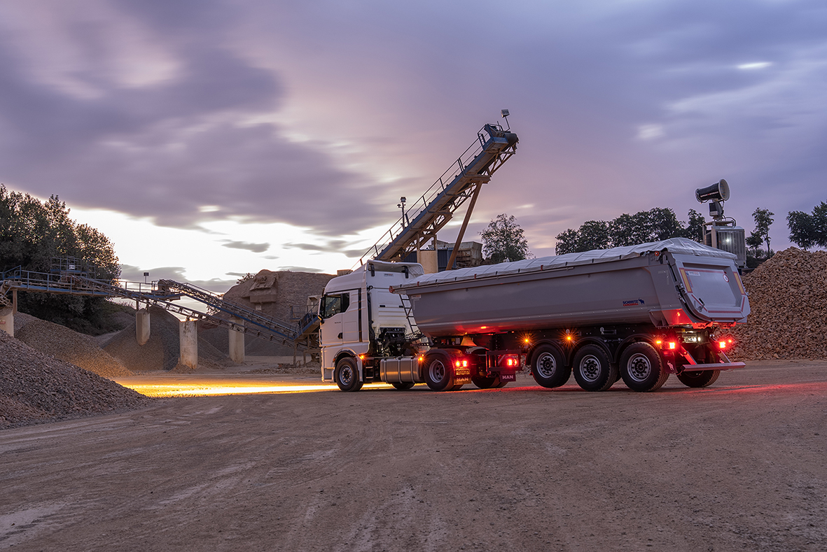 Sattelzugmaschine mit 3-Achs Sattelkipper bei Sonnenaufgang auf Baustelle