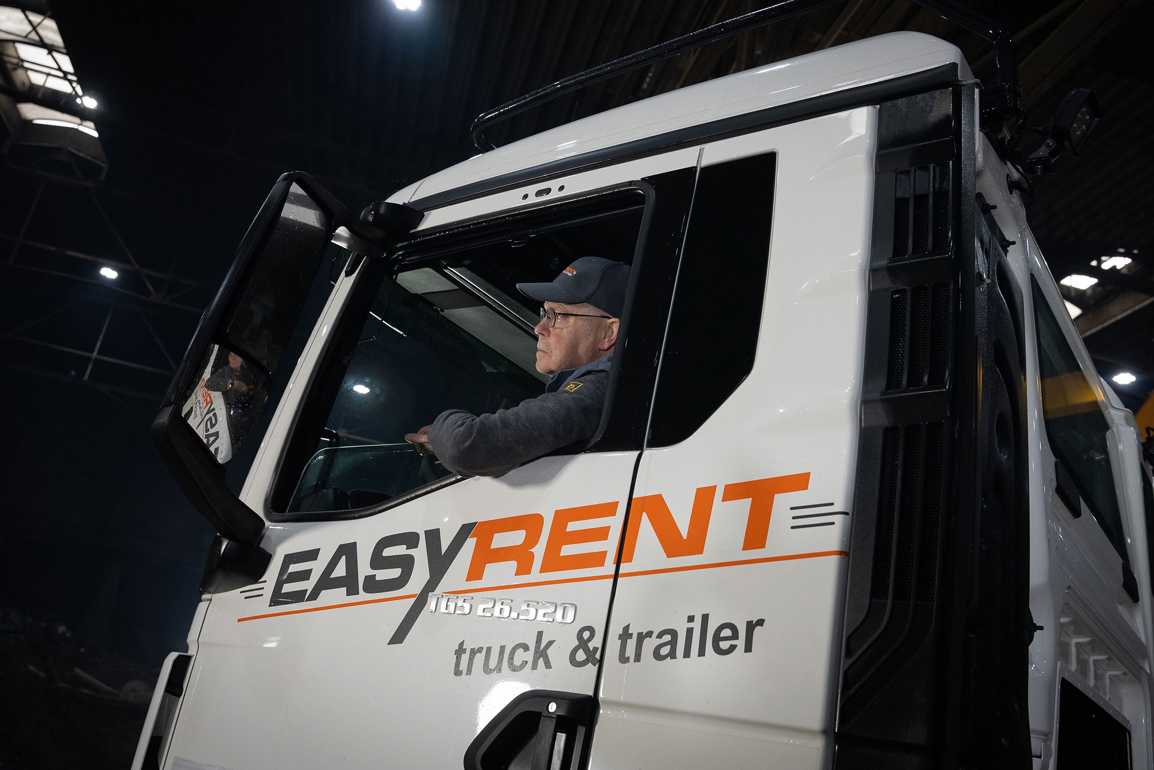 LKW Fahrer am Steuer in einem MAN LKW von Easy Rent truck & trailer blickt in den Seitenspiegel