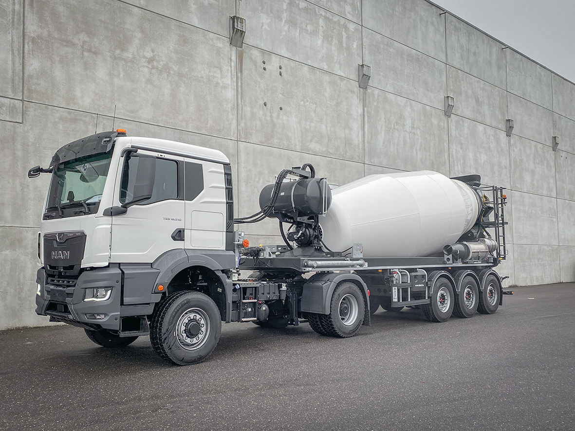 MAN tractor unit with De Buf concrete mixer trailer in front of gray wall