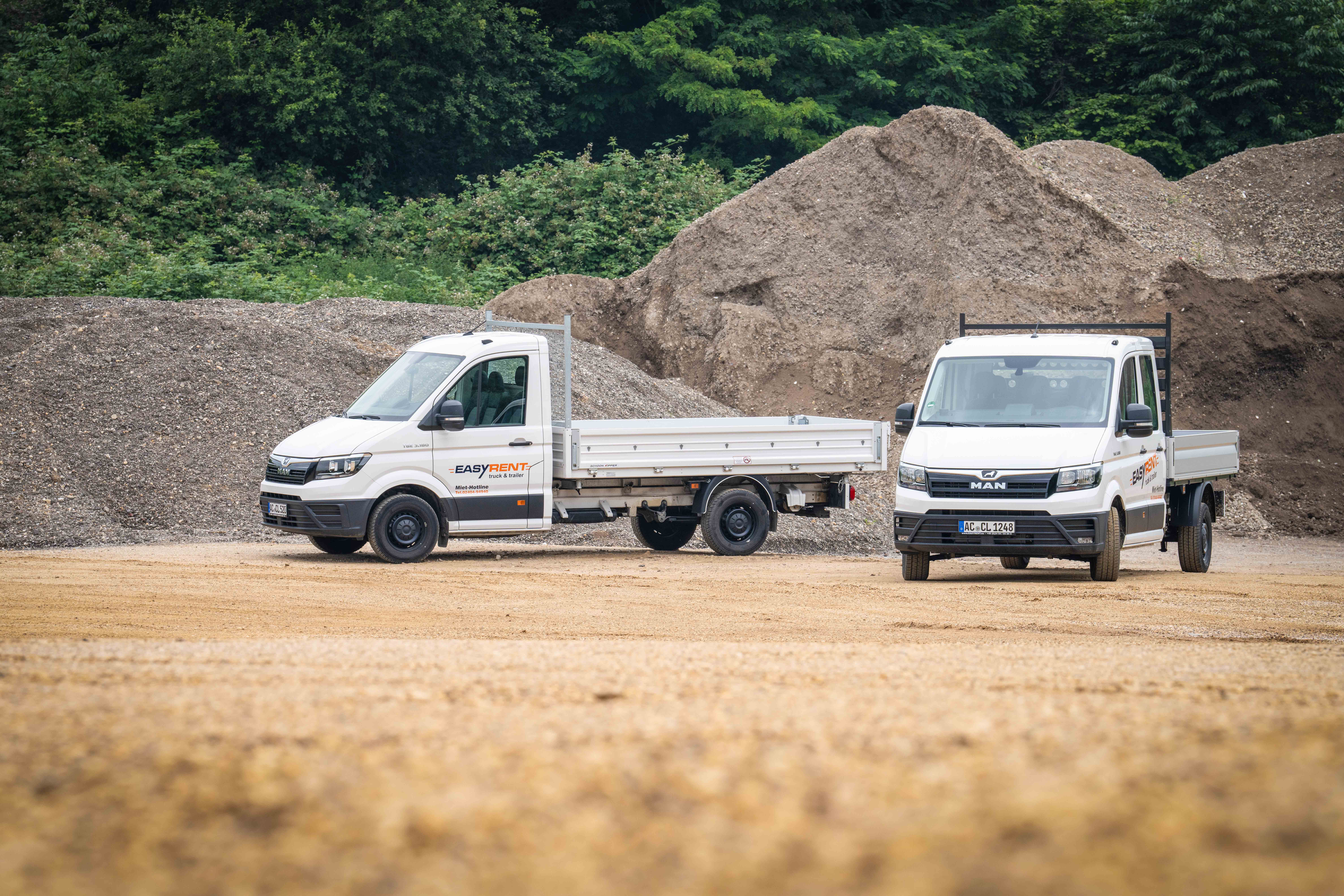 Zwei weiße MAN TGE 4x2 Transporter mit Easy Rent Beschriftung. Einer mit Pritschenaufbau und ein Dreiseitenkipper