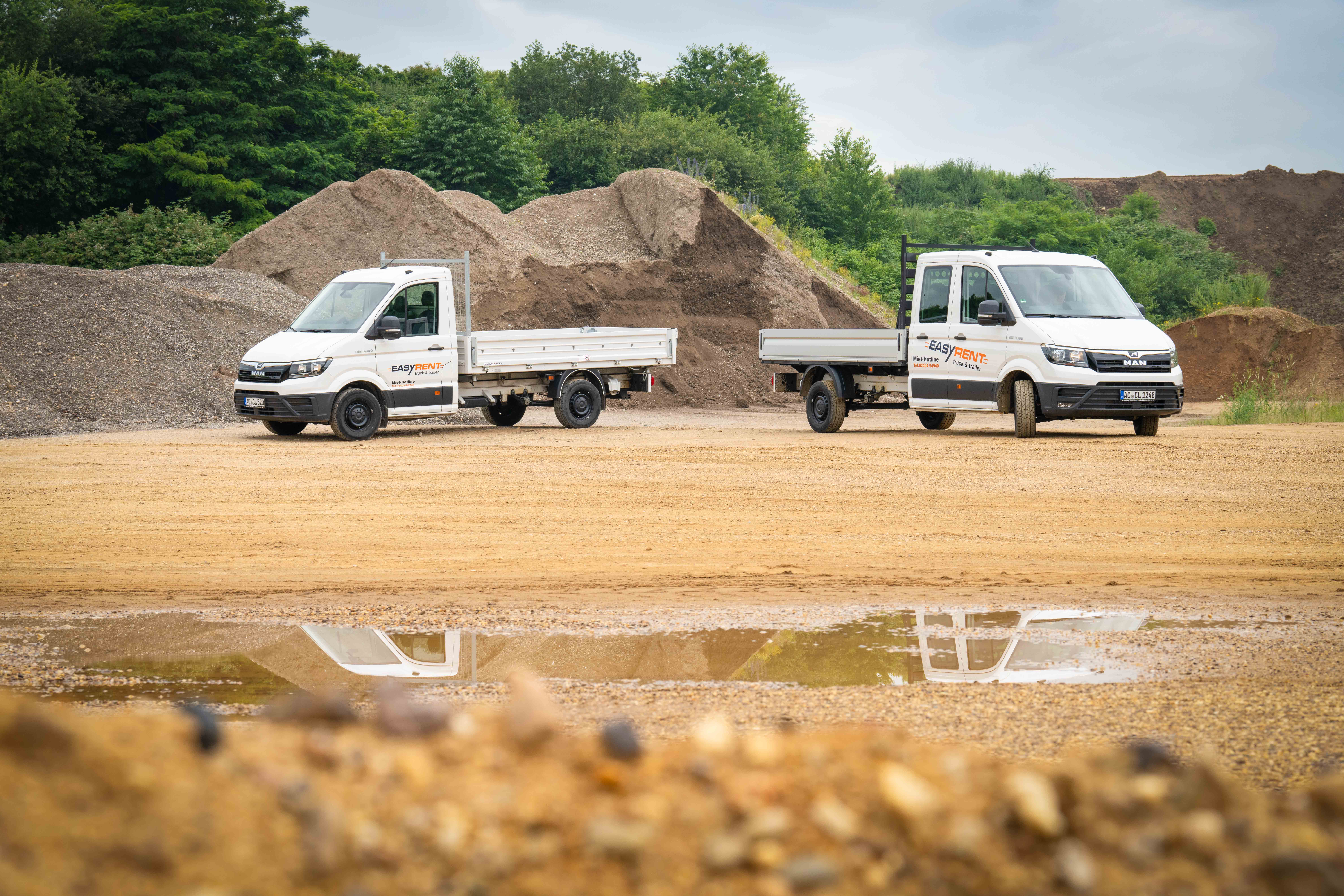 Zwei weiße MAN TGE 4x2 Transporter mit Easy Rent Beschriftung. Einer mit Pritschenaufbau und ein Dreiseitenkipper