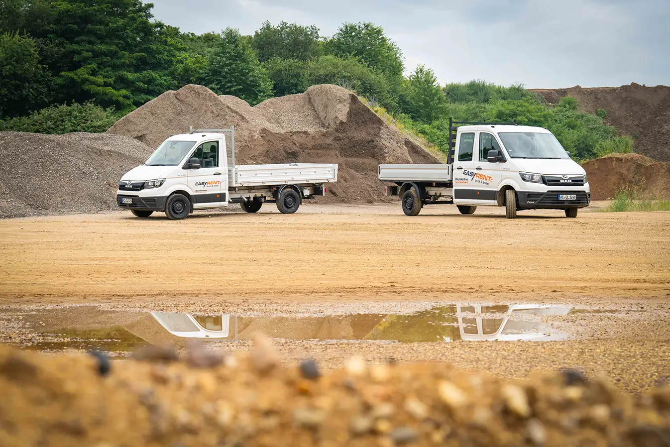 Two white MAN TGE 4x2 vans with Easy Rent lettering. One with a flatbed and a three-way tipper.