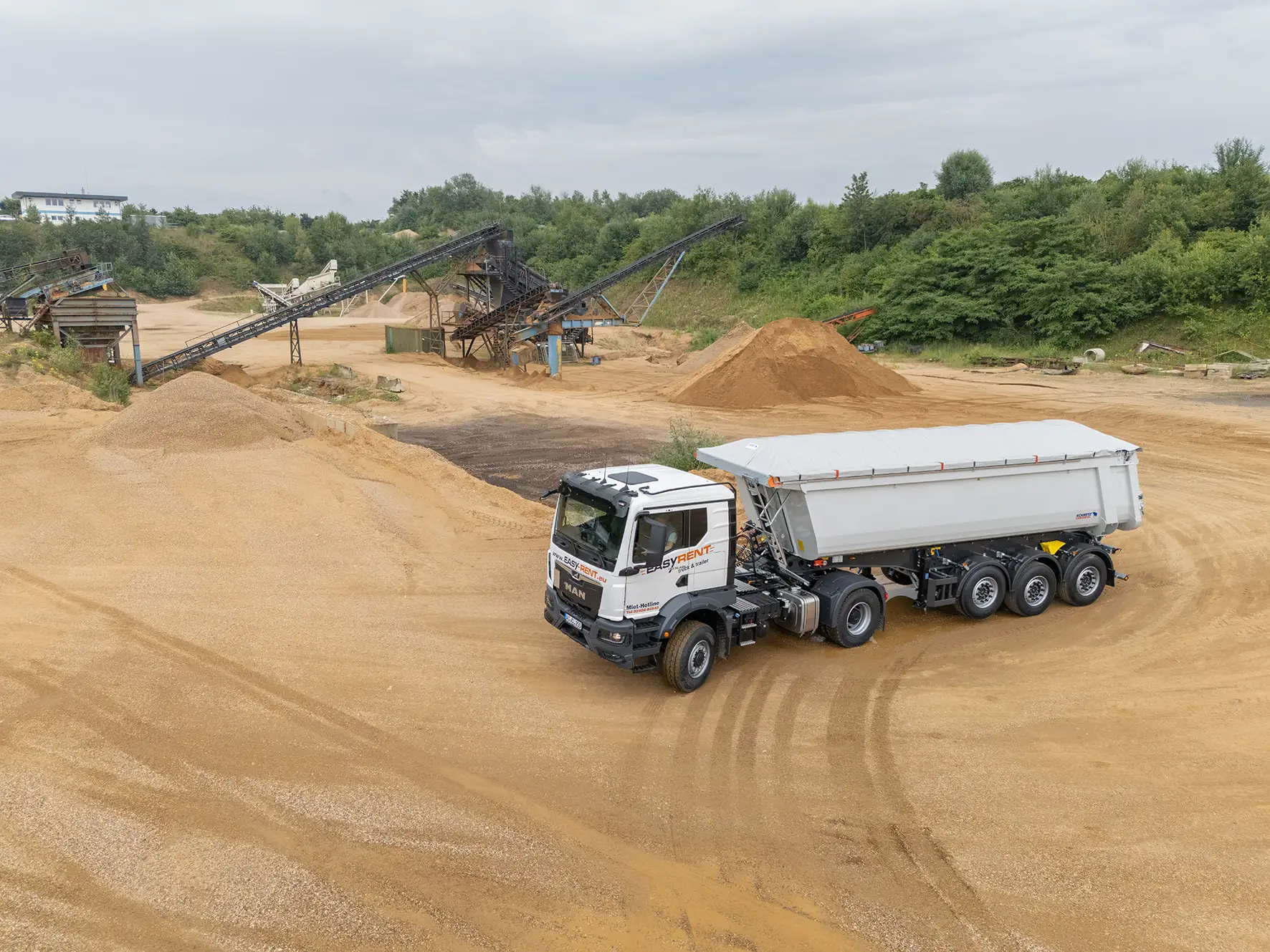 Luftaufnahme von einer MAN 4x4 Sattelzugmaschine von Easy Rent truck & trailer mit einem Schmitz Cargobull 3-Achs Stahlkipper in einer Kiesgrube