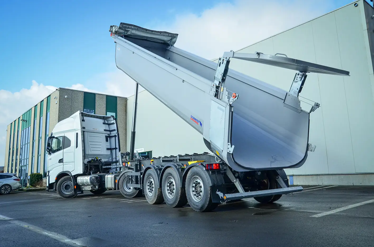 Weiße 4x2 Sattelzugmaschine mit einem Schmitz Cargobull 3-Achs Stahlkipper mit gekippter Mulde und geöffneter hydraulischer Hecktür